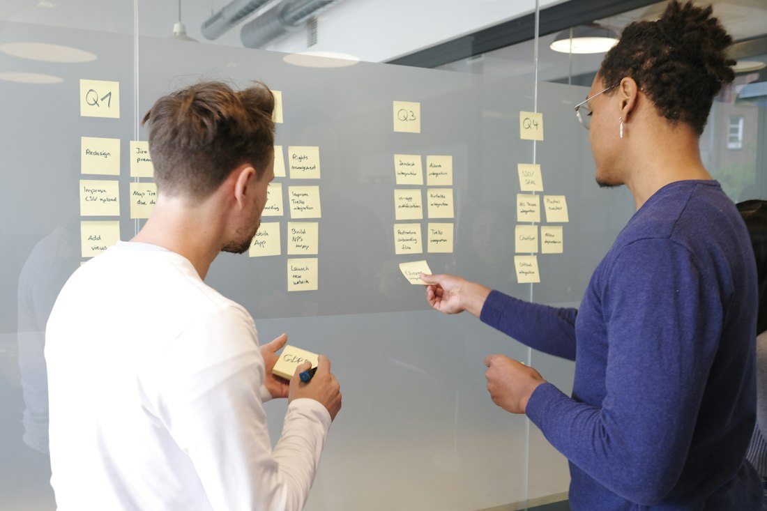 Two people mapping a process with sticky notes across a glass wall
