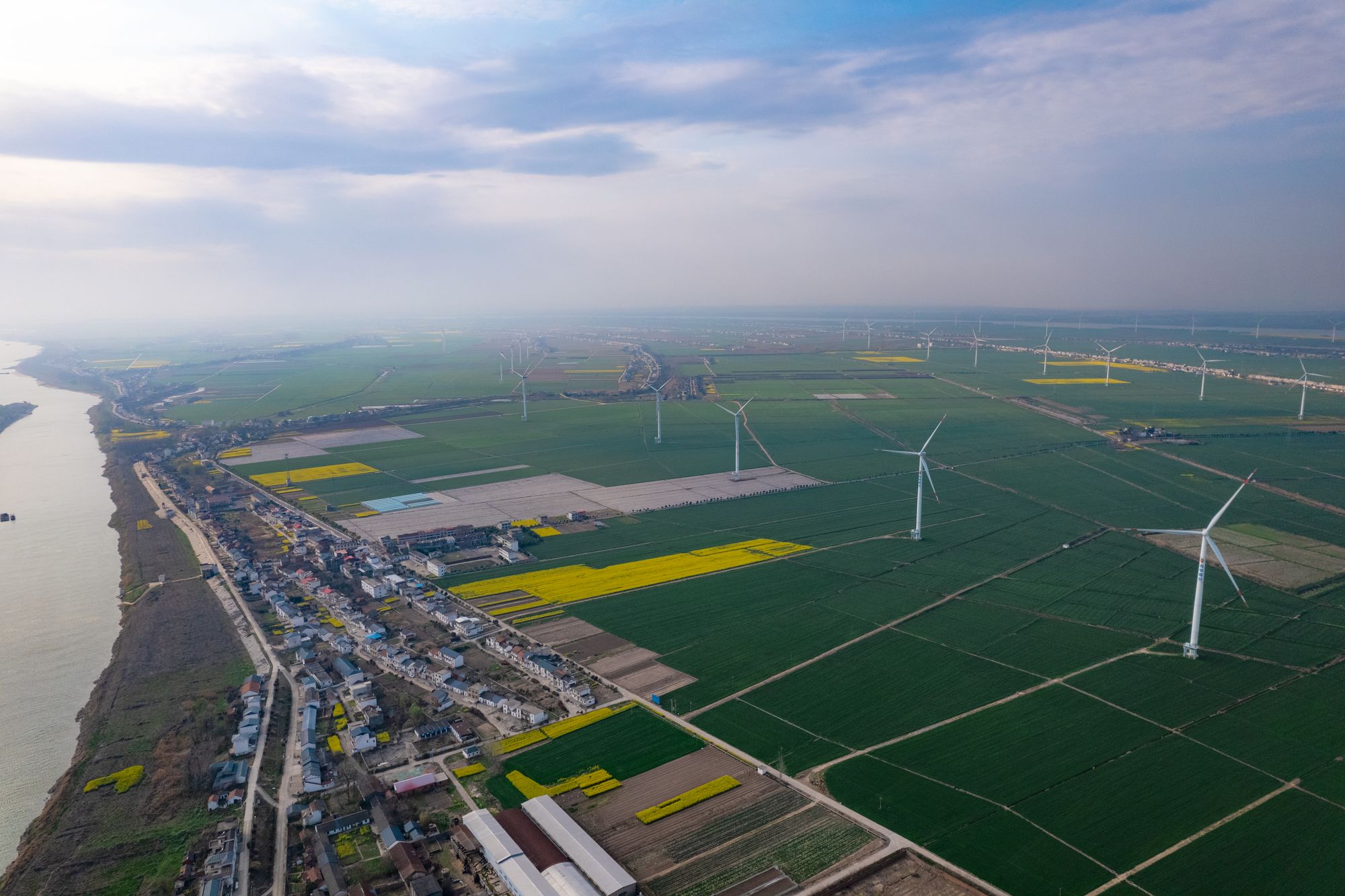 Aerial view of wind turbines standing across farmland beside a wide river