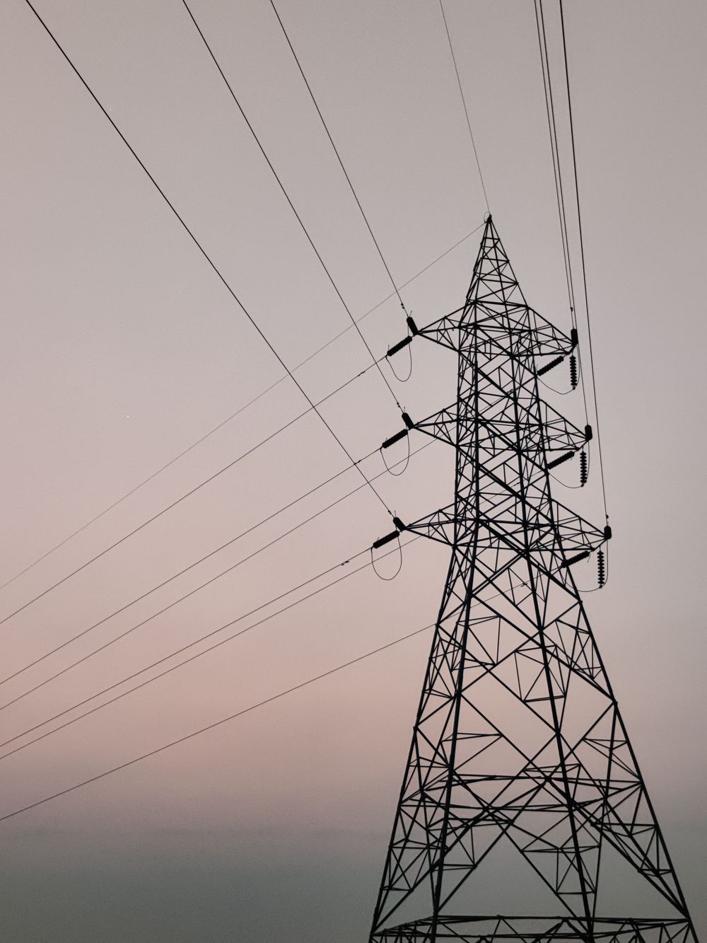A transmission tower carrying power lines against a soft dusk sky