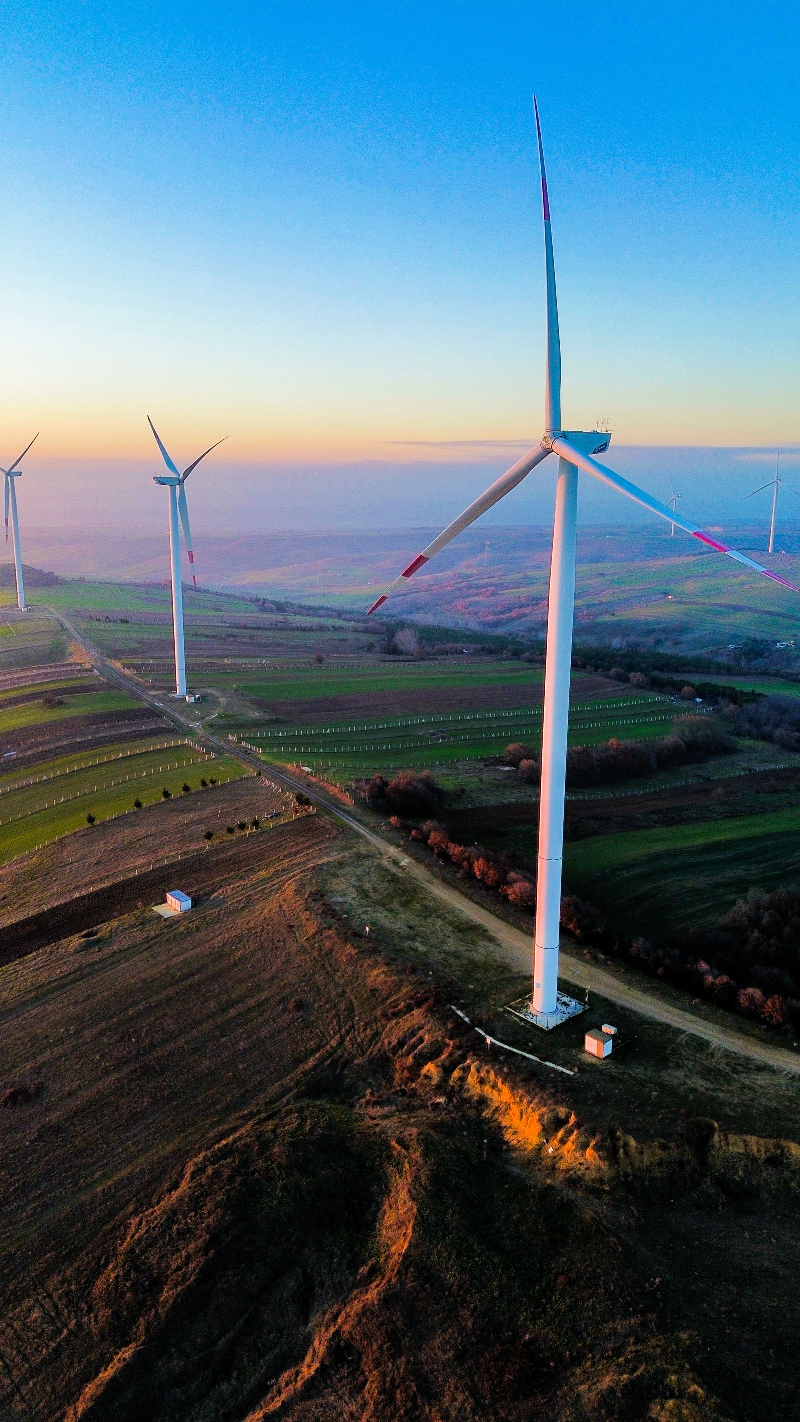 Wind turbines along a ridge above patchwork farmland at sunset